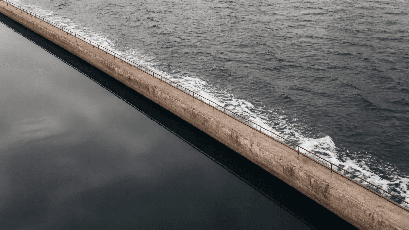 A concrete sea wall between calm and open water
